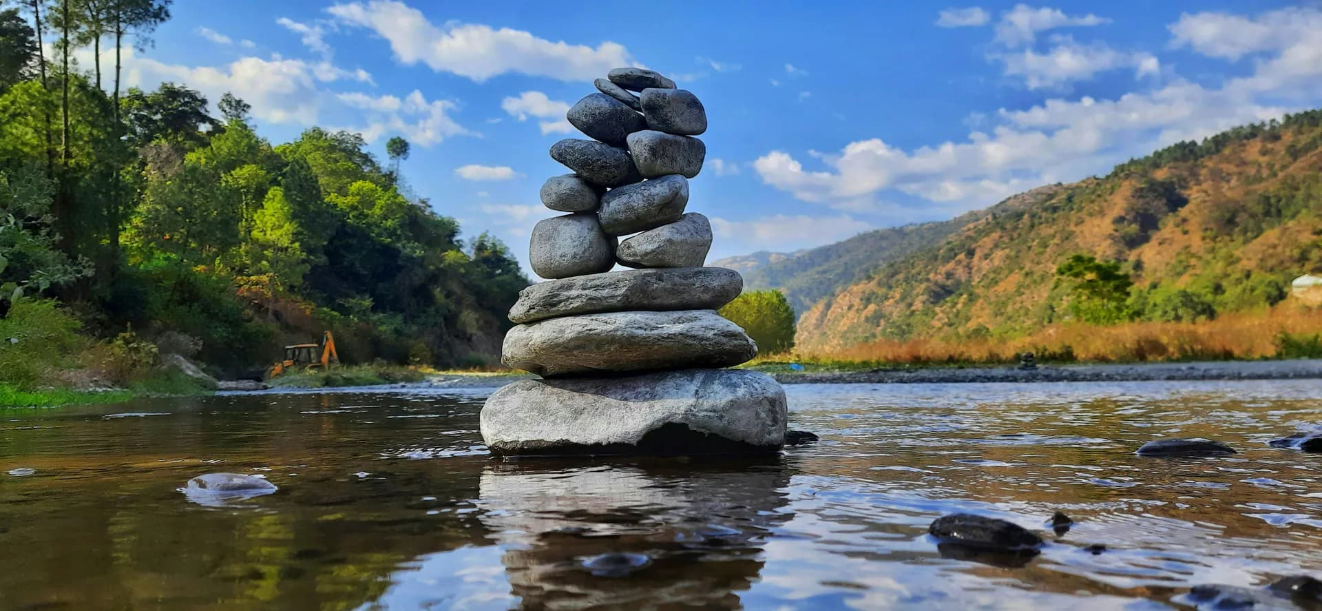 Peaceful riverbank picnic spot at Ashwani Khud with clear water and stacked river stones